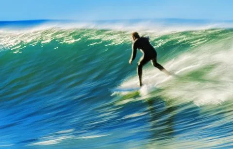 A man surfs a fast wave with dynamic motion Stock Photos