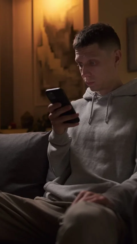 Man surprised by content on smartphone, evening home atmosphere, vertical video Video stock 314893470