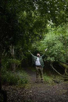 A man surrounded by nature looks up while raising his arms. Stock Photos