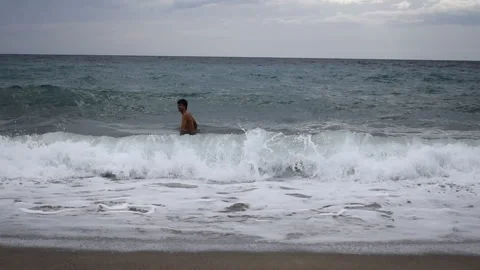 A man sways on the waves and then goes out from the raging ocean Stock Footage 240409877