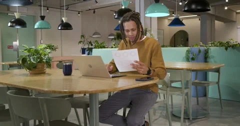 Man in sweater finding confusing pages, calling phone while typing laptop at Stock Footage 335514408