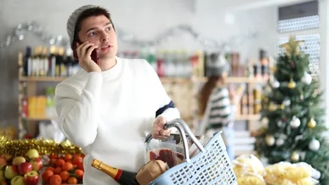 Man in sweater making mobile phone call near food shelves in Christmas Stock Footage 327133068