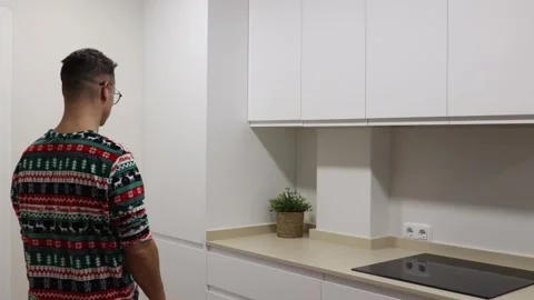 Man in a sweater stands in modern kitchen looking at wall with focus on decor an 库存影片 323606136