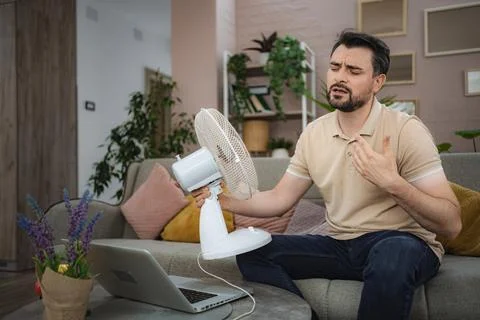 Man sweating at home refreshing himself with a fan during a heat wave Stock Photos