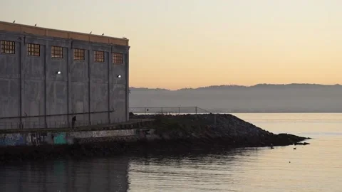 Man sweeping path by industrial warehouse on coast of San Francisco Bay Stock Footage 233902672