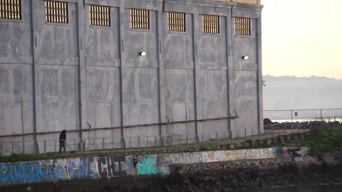 Man sweeping path by industrial warehouse on coast of San Francisco Bay Stock Footage 233902676