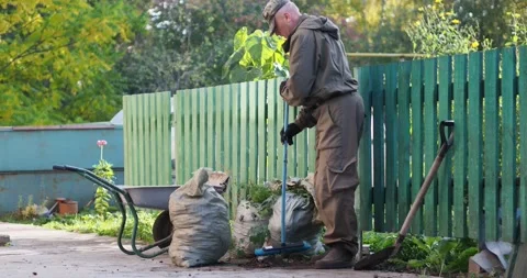 A man sweeps the sidewalk with a brush, there are filled garbage bags nearby. Stock-Footage 161073331