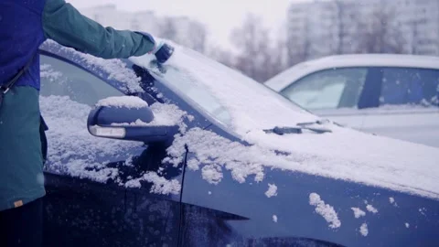 Man sweeps snow from a car windshield with a hand broom Stock Footage 145459747