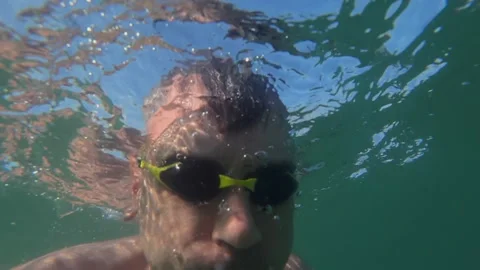 Man swimming with goggles, creating surface water reflection and distortions Stock Footage 339795237