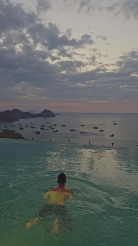 Man swimming in infinity pool enjoying sunset view of komodo island Stock Footage 346544745