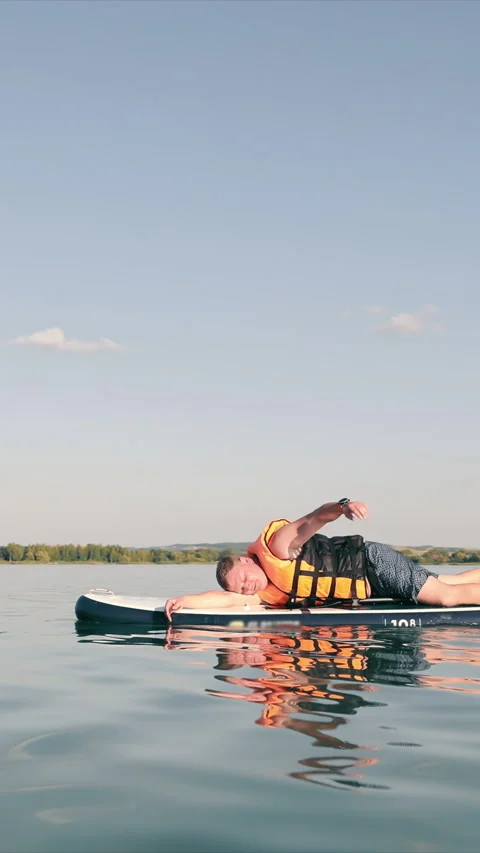 A man swimming lying down on a SUP board and rowing with one hand. The sky and Video stock 313291549