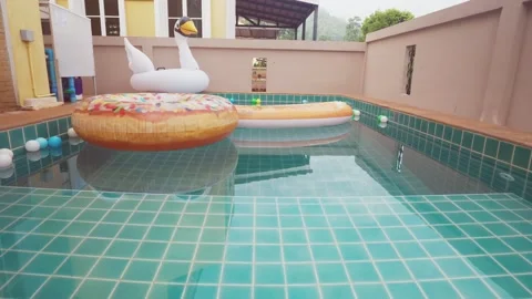 A man is swimming in a pool with a pool float shaped like an orange Stock Footage 315929436