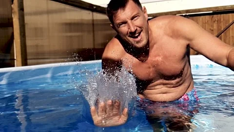 A man in a swimming pool splashes water over the camera in super slowmotion Stock Footage 137574853