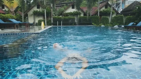 Man swimming in resort pool, surrounded by tropical lush greenery, enjoying Stock Footage 295054876