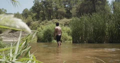 Man in swimming trunks in a river  raises his arms in nature Stock Footage 136029662