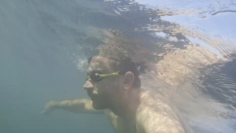 Man swimming underwater with goggles, looking up at the water surface reflecting Stock Footage 343197075