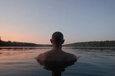 A man swims in a forest lake in the evening. Back view. Alone with nature. Foto stock