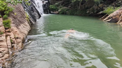 Man swims pristine natural pool under waterfall. Outdoor lifestyle essential for Stock Footage 322218146