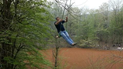A man swinging at a height in a forest with a red beautiful lagoon in background Stock Footage 97033938