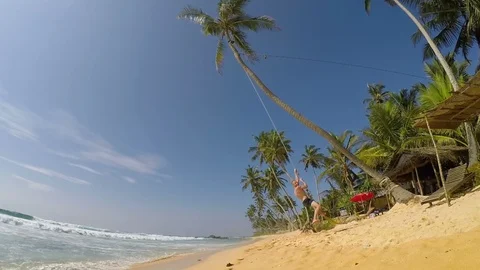 A man swinging on the palm tree on the white beach. Exotic vacation holidays  Stock-Footage 99072852