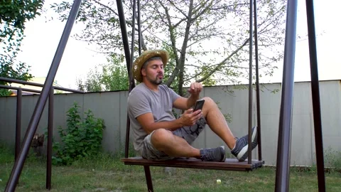 Man swinging on a swing and talking via video link 4K Stock Footage 160110258