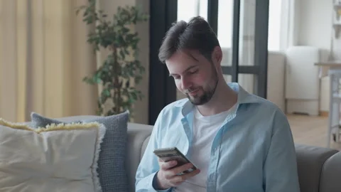 Man Swiping Through Smartphone Content On Bright Cozy Living Room Sofa Stock Footage 318947417