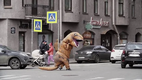 Man in t rex costume running at city street crosswalk Stock Footage 84930401
