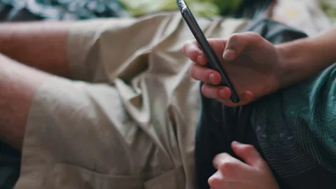 Man in a T-shirt and shorts is lying on the couch and is holding a smartphone Stock Footage