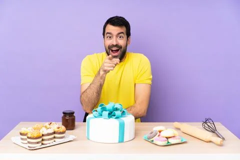 Man in a table with a big cake surprised and pointing front Stock Photos