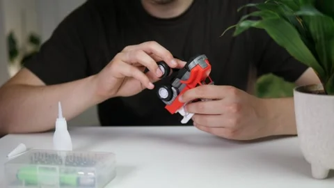 A man at a table with a broken car, tools and glue, trying to figure out how to Stock Footage 314033878