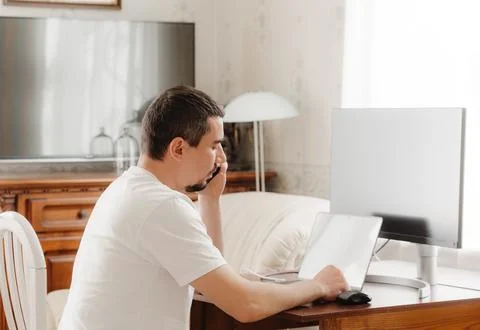 A man at a table with a computer talking on the phone Stock Photos