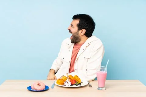 Man at a table having breakfast waffles and a milkshake laughing in lateral p Stock Photos