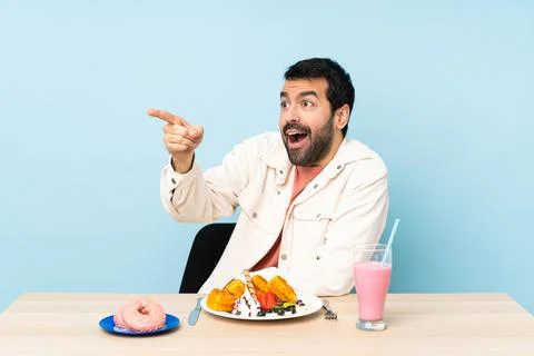 Man at a table having breakfast waffles and a milkshake pointing away Foto stock