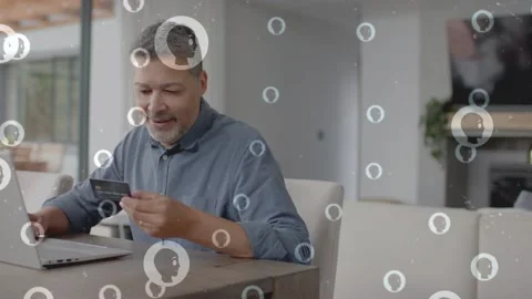 Man at table holding credit card, paying on laptop, overlay icons drifting Stock Footage 333463781