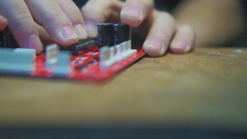 A man on a table inserts a microcircuit into a red electronic board close-up Видео 231799610