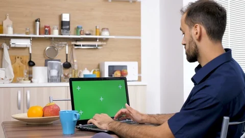 Man at the table in the kitchen drinking coffee and typing on computer Stock Footage 97276922