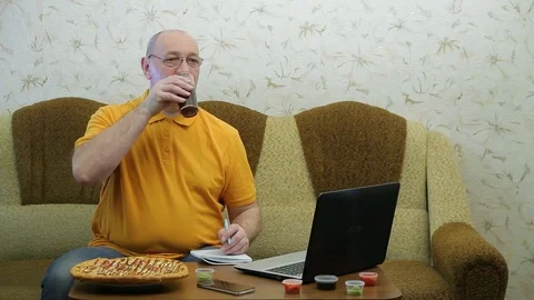 A man at a table with a laptop is finishing work before a pizza dinner Stock Footage 126984275