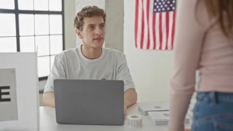 Man at table with laptop hands ballot to woman over clear ballot box in vot.. Stock Footage 337440878