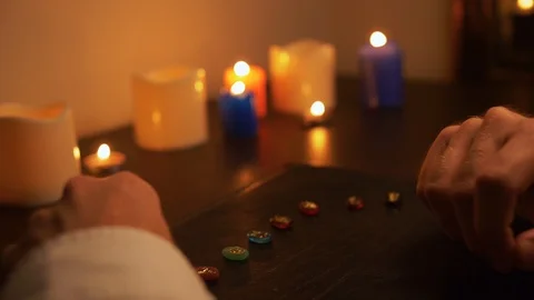 Man at table lays out colored stones on a black cardboard. Candles are burning. Video stock 105736114