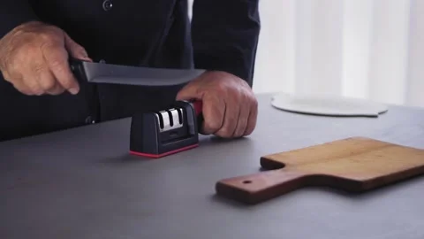A man at the table sharpens a kitchen knife in a knife sharpener Stock Footage 249888228
