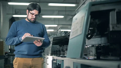 Man with a tablet computer is inspecting a functioning printing equipment Video stock 105152604