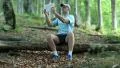 Man with tablet computer sits on a fallen tree in the forest HD Footage