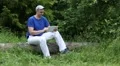 Man with a tablet computer sits on a fallen tree in the forest HD Footage