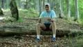 Man with tablet computer sits on a log in the forest HD Footage