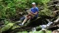 Man with tablet computer sits near small river in forest HD Footage