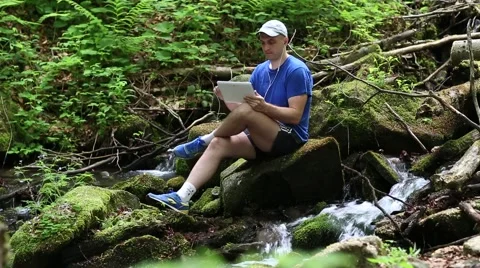 Man with tablet computer sits near small river in forest 스톡 동영상 54042255