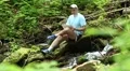 Man with tablet computer sits near small river in forest HD Footage