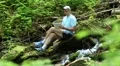 Man with tablet computer sits near small river in forest HD Footage