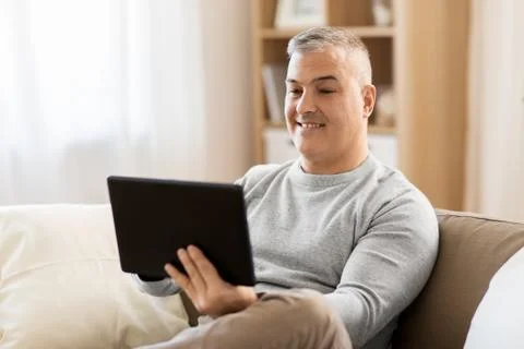 Man with tablet pc sitting on sofa at home Stock Photos