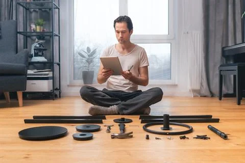 A man on a tablet is watching a video tutorial on self-assembly of furniture. Fotos Stock